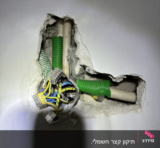 חוטי חשמל צבעוניים בצינור ירוק בקיר שבור